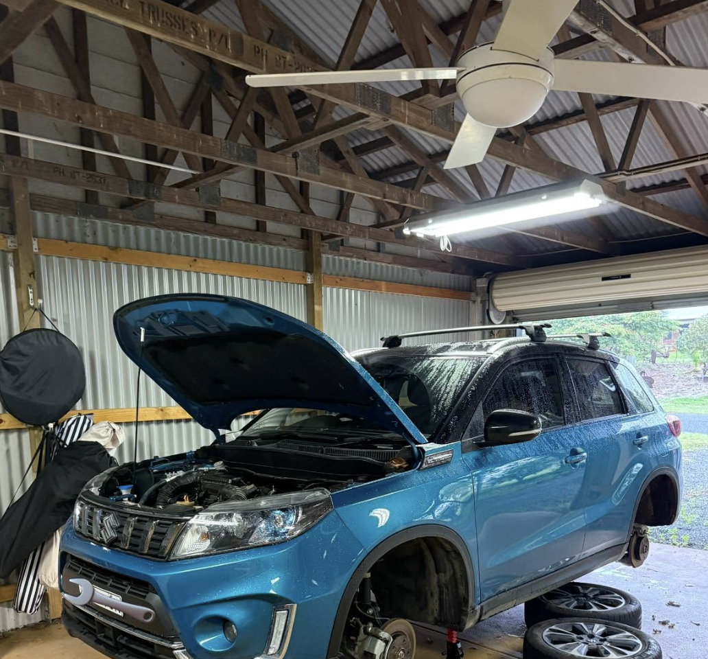 Blue Suzuki Vitara with bonnet open and wheel removed under a carport during a mobile service - Meek Mobile, Newcastle